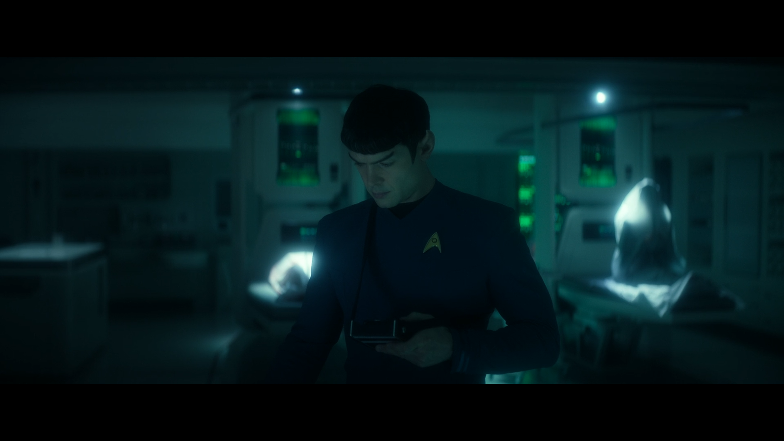 Spock looking at his tricorder while a shape in a bodybag sits up on a bio bed behind him